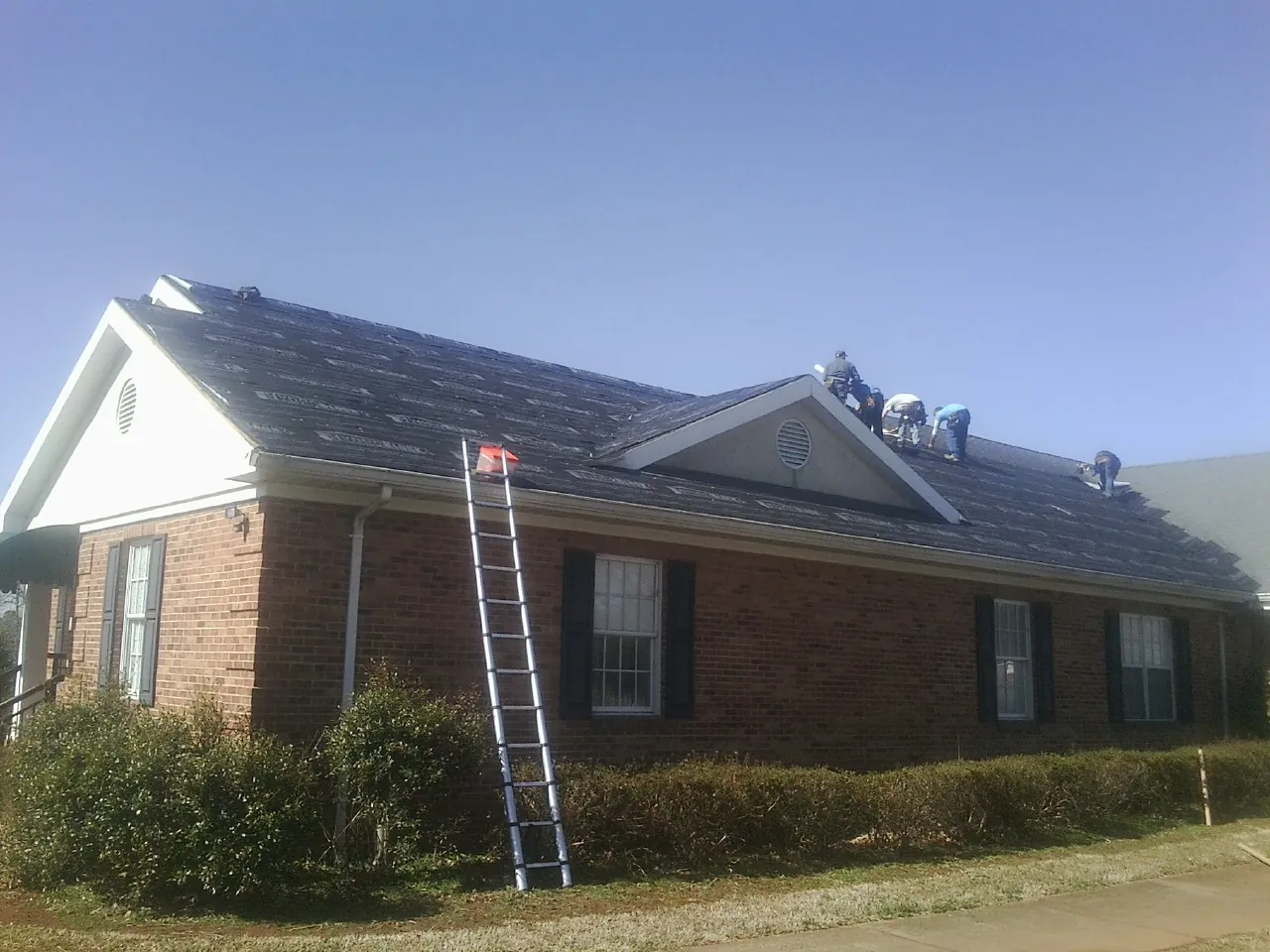 Crew tearing shingles off a brick ranch roof with a ladder set — Metal Roof Repair work by our crew in Excelsior