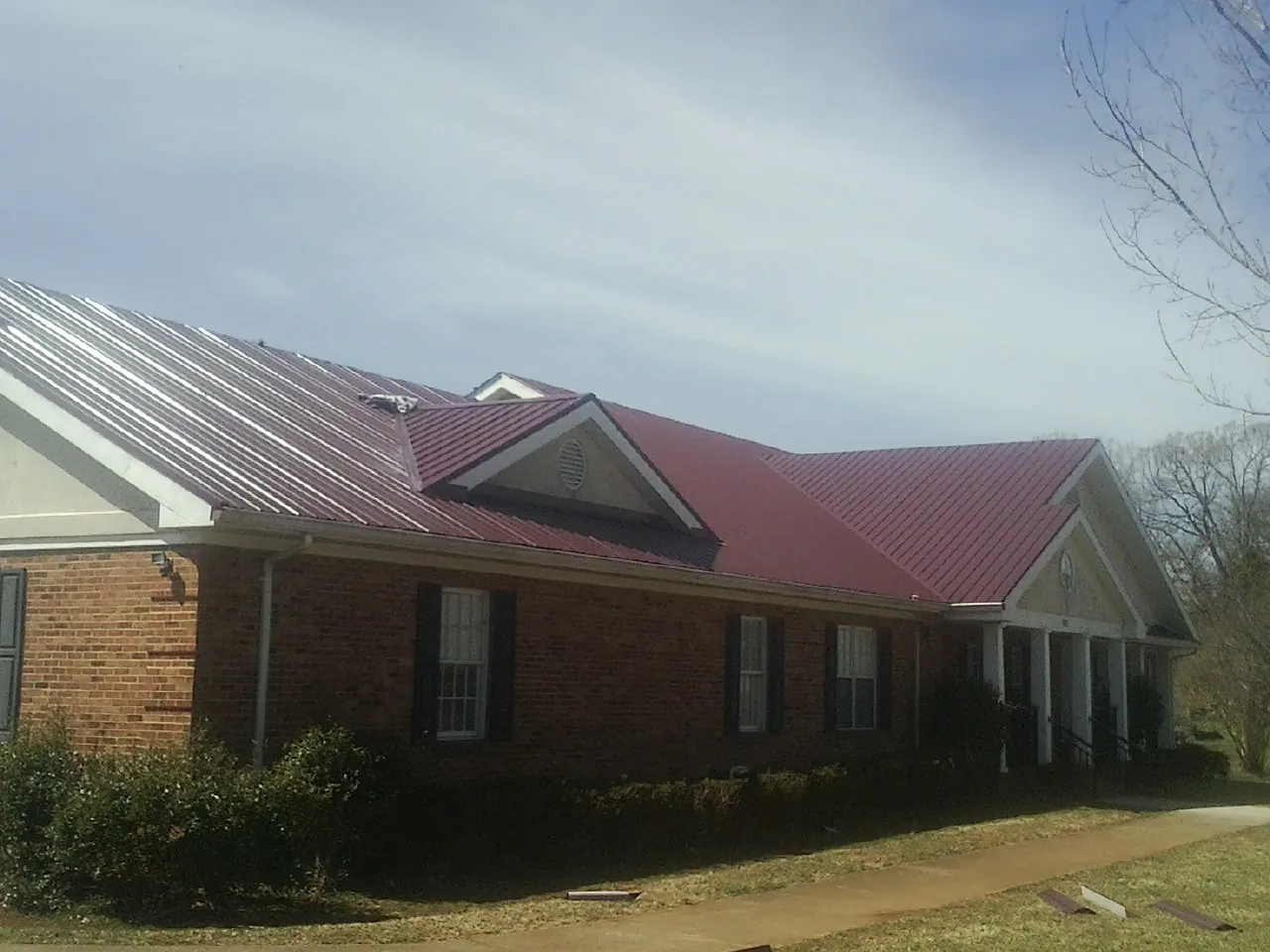 Red metal roof with gabled entries on a long brick building, from a Hail Damage Roof Repair job in Excelsior