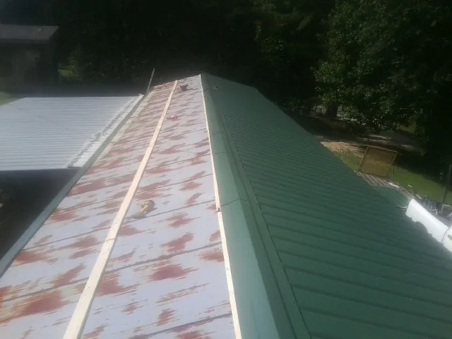 Old rusted panels beside newly installed green metal roofing — Wind Damage Roof Repair by Roofing Brothers in Excelsior