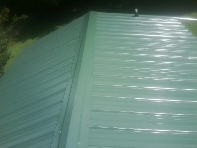 New green metal panels meeting at the ridge of a roof — Flat Roof Repair work by our crew in Excelsior