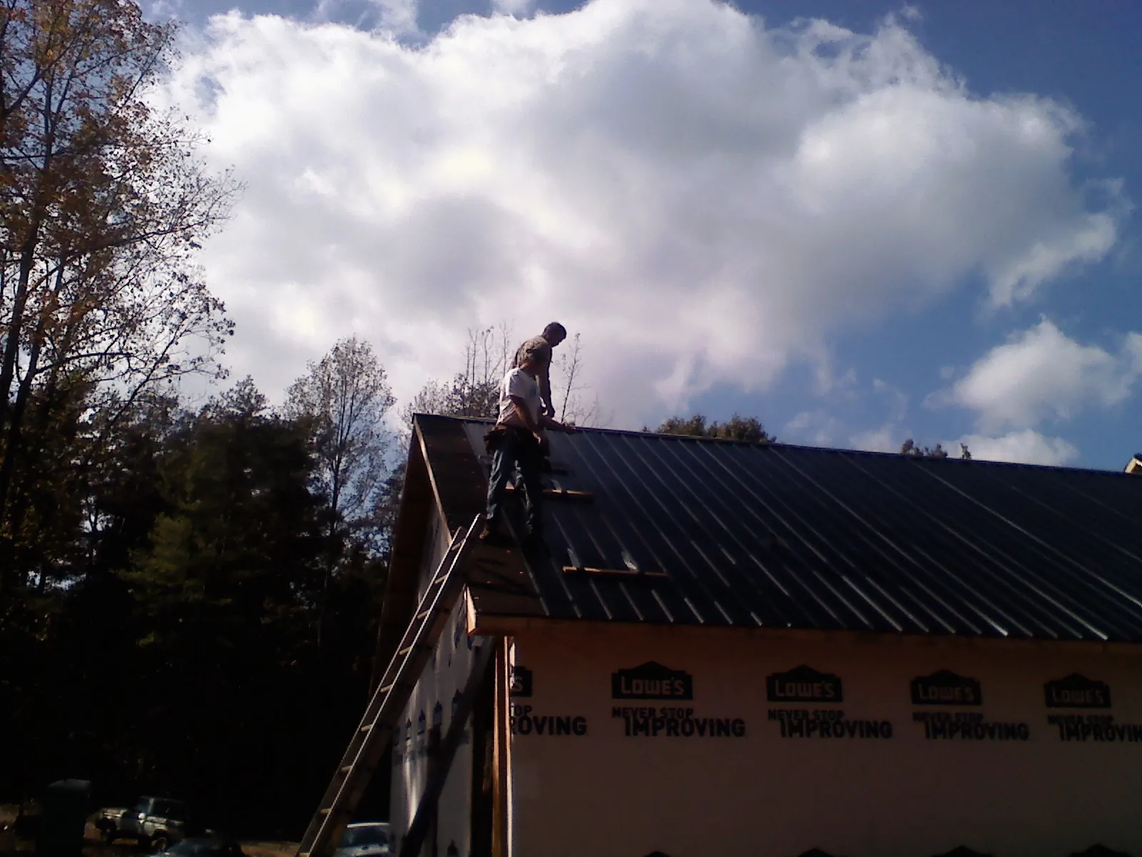 Roofer fastening dark metal panels high against a cloudy sky, from a Roof Inspection job in Excelsior